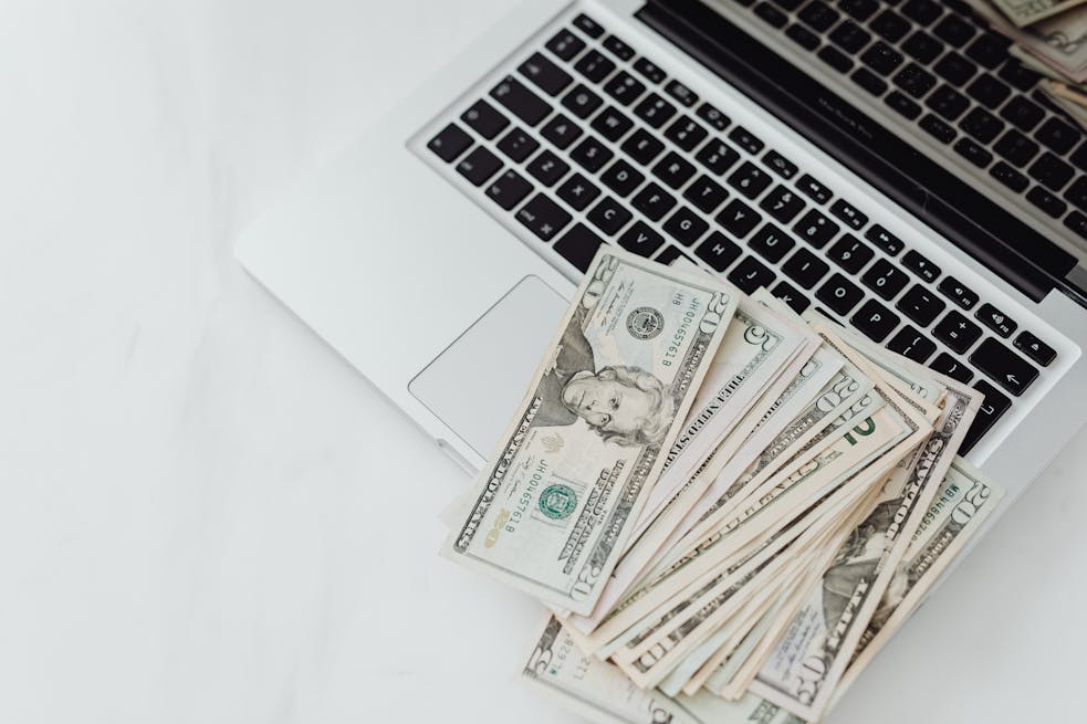 A stack of US dollar bills on a laptop keyboard representing online finance and budgeting.