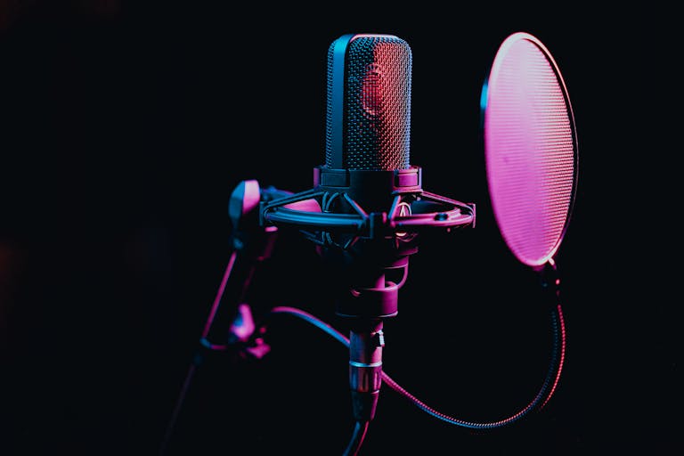 Close-up image of a condenser microphone with a pop filter in a studio setting, featuring atmospheric lighting.