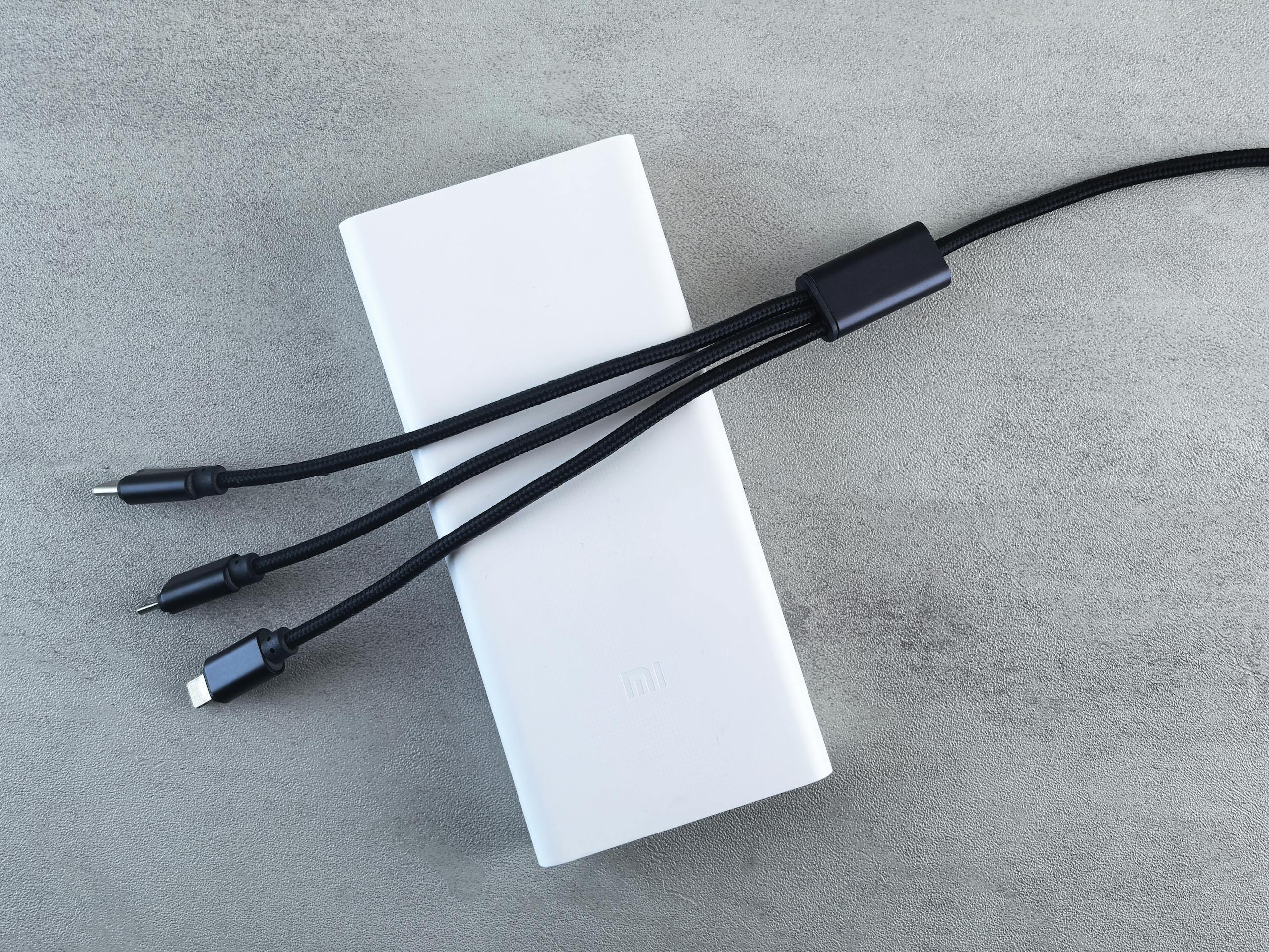A sleek white power bank with a black multi-connector cable laid on a textured grey surface, emphasizing modern technology.