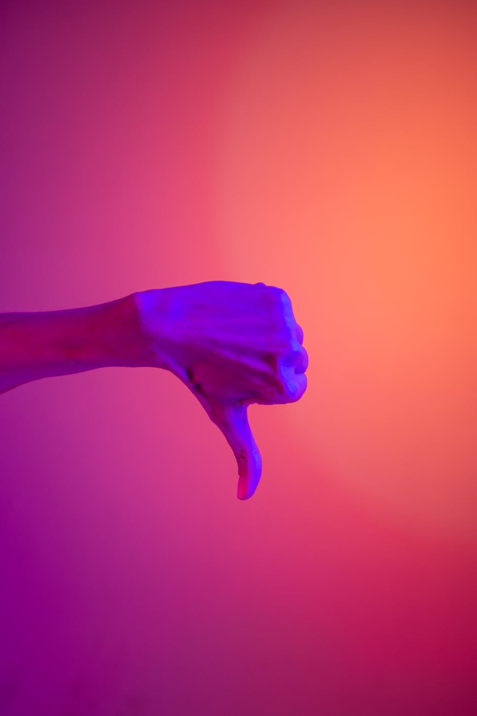A hand showing a thumbs down sign with vibrant neon purple and orange lighting.