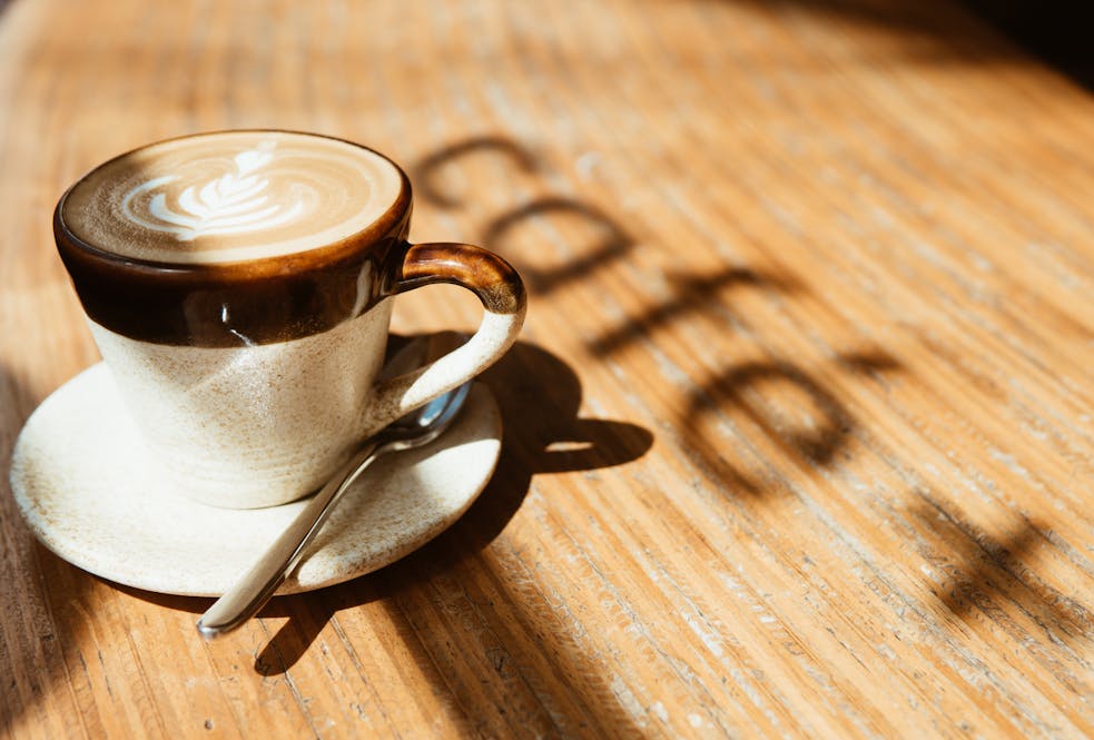 A warm cappuccino with latte art basking in morning sunlight on a wooden table.